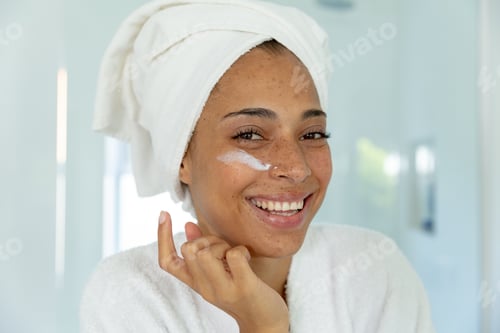 Preview: Mixed race woman wearing bathrobe and cleansing face mask in bathroom