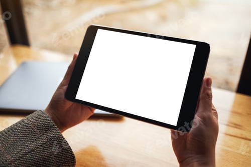 Preview: Mockup image of a woman holding black tablet pc with blank white screen with laptop on wooden table