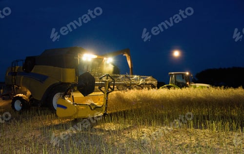 Preview: Combine harvester and grain trailer working at night under lights.