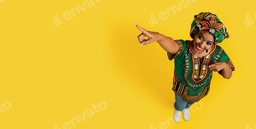 Preview: Cheerful pretty young black woman in traditional outwear showing ad