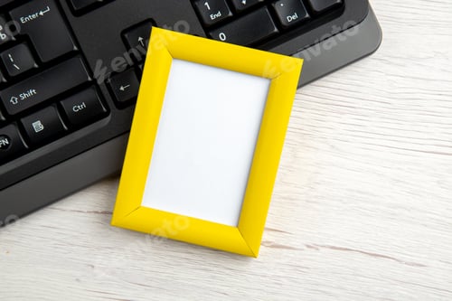 Preview: Top view of yellow empty picture frame on half shot laptop on white stripped background