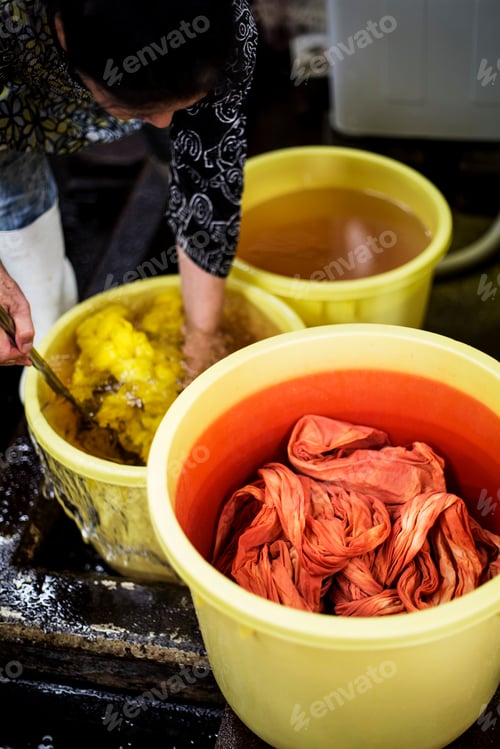 Preview: High angle view of bright yellow and orange fabric in plastic buckets in a textile plant dye