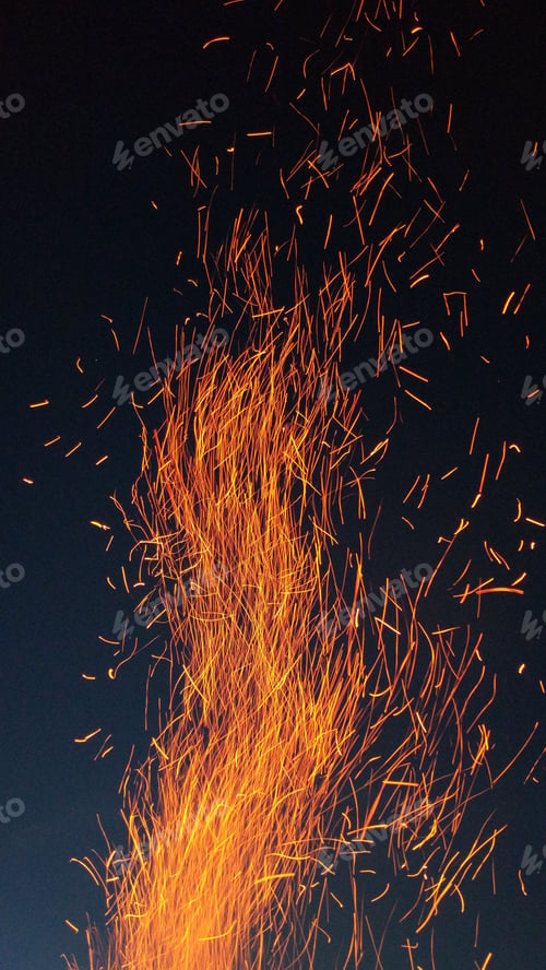 Preview: Vertical shot of flames of fire with flying burning red sparks against the dark night sky