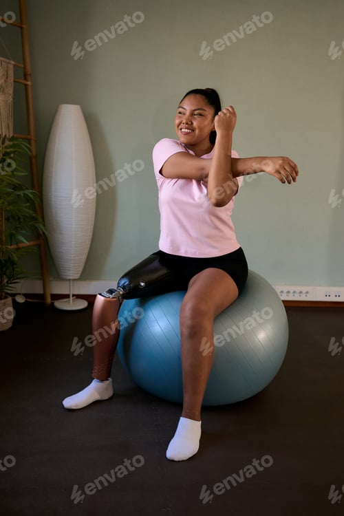 Preview: Young woman with prosthetic leg exercising on fitness ball