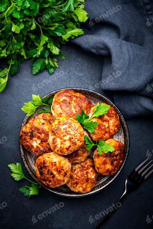 Preview: Homemade meatballs with spices and parsley in ceramic bowl, black table background, top view