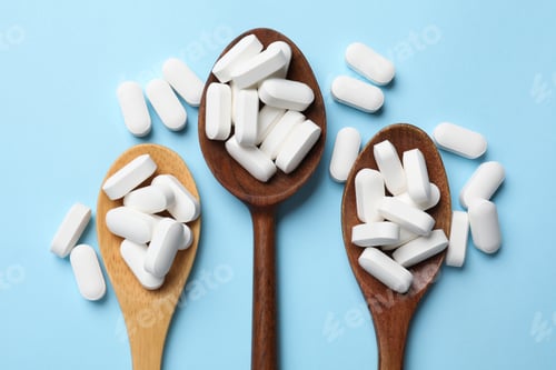 Preview: Vitamin capsules in wooden spoons on light blue background, flat lay