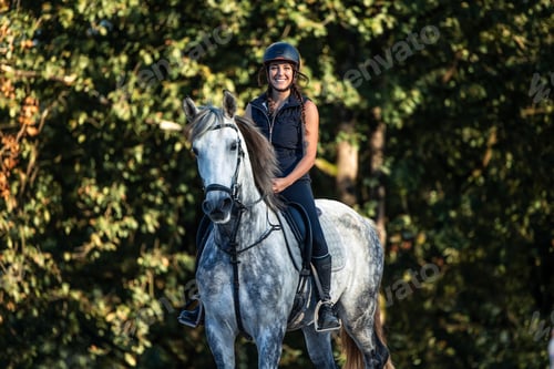 Preview: Young female rider smiles at the camera while horseback riding through the forest