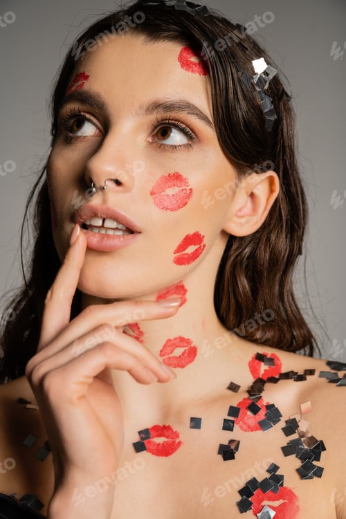 Preview: sexy and dreamy woman with red kisses on face and body touching lip and looking away isolated on
