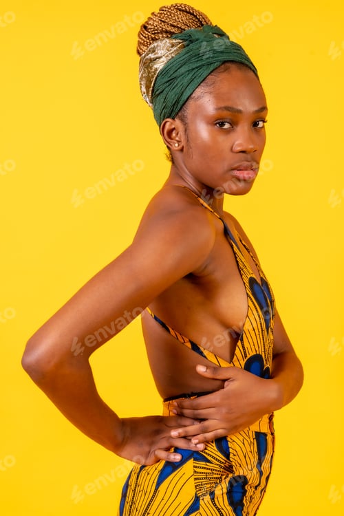 Preview: African young woman in the studio on a yellow background, traditional costume, serious look