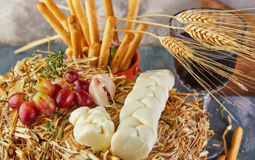 Preview: Pigtail-shaped mozzarella with grapes in the hay with bread ears on a blue background.