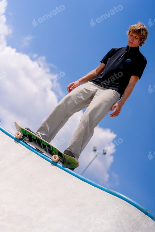Preview: A young guy skater stands on the edge of a skate pool against a backdrop of sky and clouds