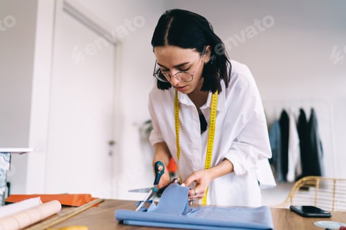 Preview: Focused woman standing near table with scissors in hand and fabric