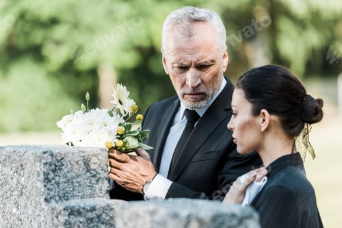 Preview: selective focus of upset man holding flowers and standing near woman in cemetery