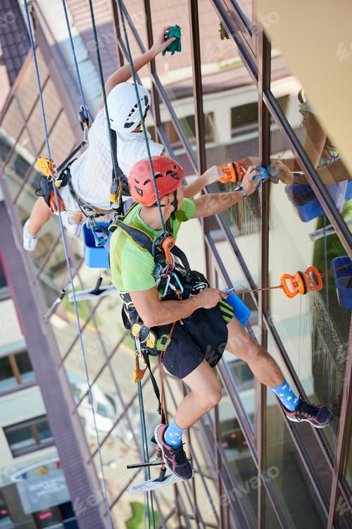 Preview: Industrial mountaineering worker cleaning window outside building.