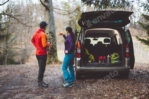 Preview: A woman packing clothes into a car, smiling and focused. She wears a purple jacket and a bandana, wi