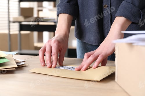 Preview: Woman putting barcode onto envelope at table in post office, closeup