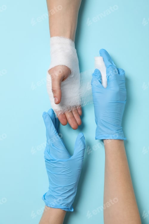 Preview: Concept of help during an injury, doctor wrapping hand in bandage on blue background