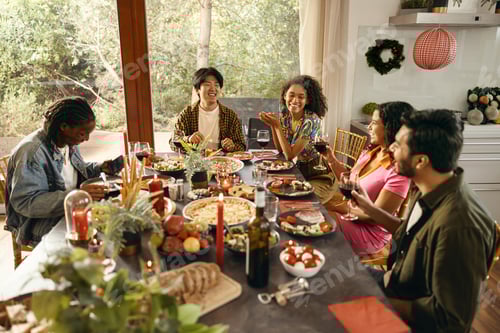 Preview: Happy friends enjoying in conversation and drinking wine during festive dinner at home party