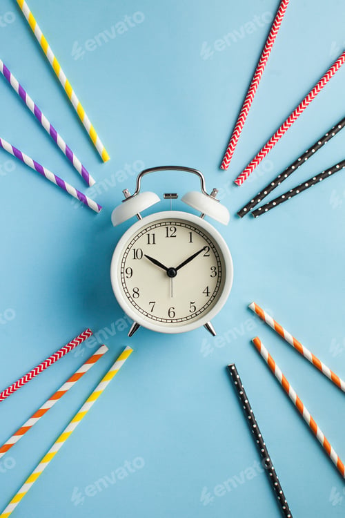 Preview: alarm clock around multi-colored paper tubes for cocktails on a blue background.