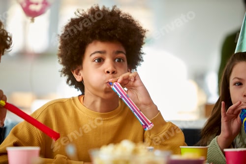 Preview: Boy Celebrating Birthday With Party Blower At Party With Friends At Home