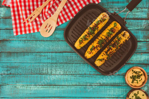 Preview: top view of roasted corn on grill pan and on blue wooden table with spatulas and sauces