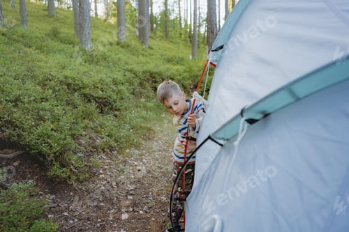 Preview: cute little caucasian boy putting up a tent. Family camping concept