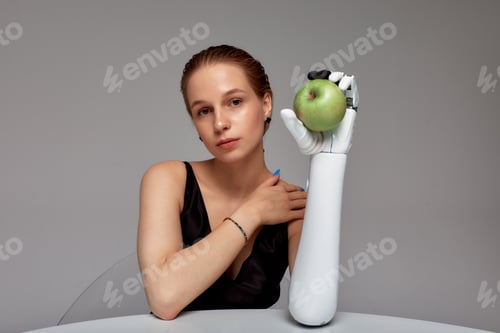 Preview: Young smiling girl with disability wearing sensory bionic prosthetic arm seats at the table