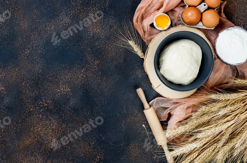 Preview: Raw yeast dough in bowl and ingredients, eggs, flour, ears of wheat on dark table, bakery concept