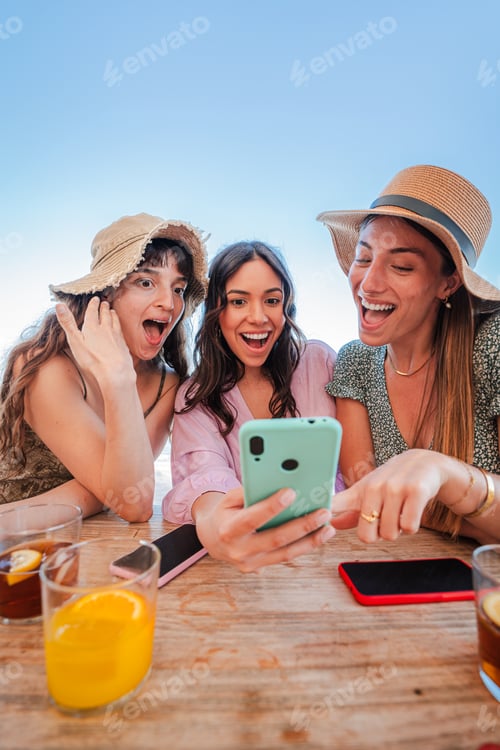 Preview: Vertical. Group of three youn women sharing on the social media using a cellphone. Girls showcasing