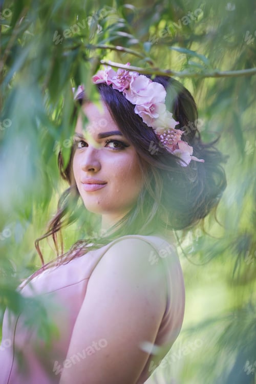 Preview: Portrait of an attractive Caucasian female wearing a floral headband seen through tree leaves