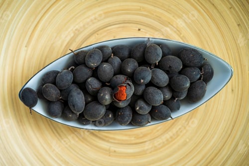 Preview: Velvet tamarind fruit ( Dialium cochinchinense) or buah keranji in a wooden bamboo plate background.