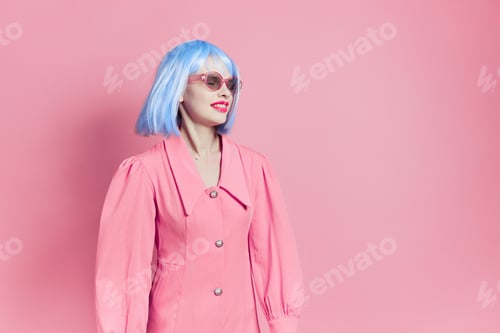 Preview: pretty woman in sunglasses wears a blue wig makeup pink background