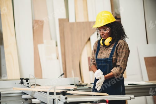 Preview: Female carpenter wearing safety goggles and hard hat for woodworking in small business workshop.
