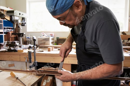 Preview: A bow maker working on a wooden bow in his workshop.