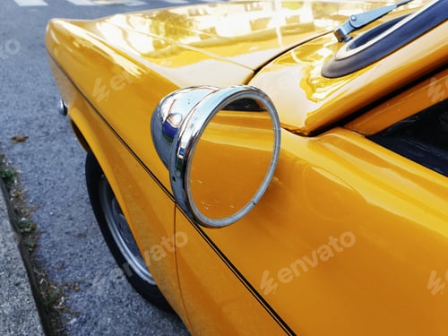 Preview: Close-up cropped image of side view mirror on a vintage yellow car.