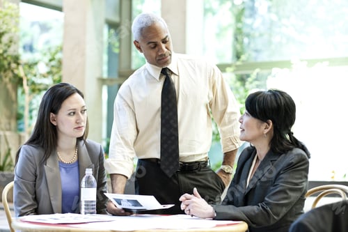 Preview: Mixed race group of three people in an informal meeting around a table in a lobby area.
