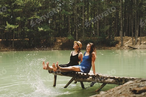 Preview: two young women are sitting on a wooden bridge on the lake