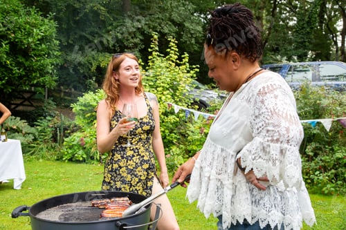Preview: Women enjoying a summer BBQ garden party cooking and eating outside