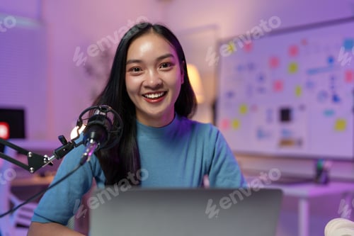 Preview: Young asian female podcaster smiling and recording audio podcast at home studio using professional m