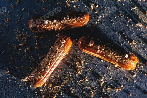 Preview: Caramel eclairs with golden sprinkles on dark bakcground.