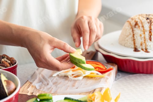 Preview: Woman preparing spring rolls in rice paper on kitchen table.