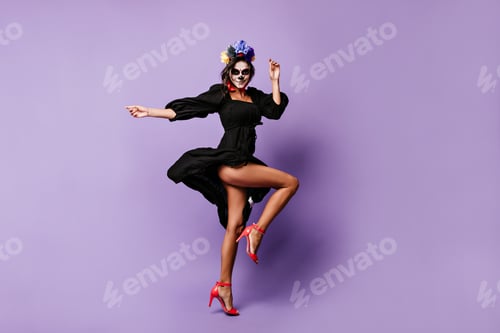 Preview: Smiling girl with flowers in dark hair is dancing coquettishly, posing in black dress on isolated b