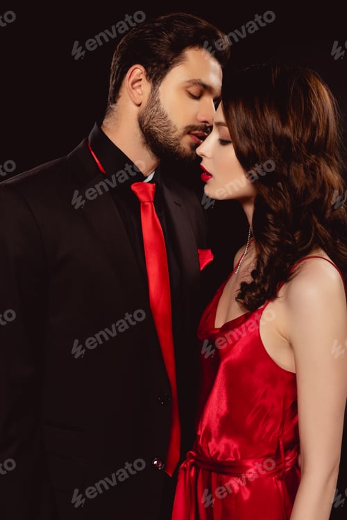 Preview: Side view of handsome man kissing beautiful girlfriend in dress isolated on black