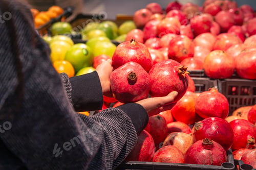 Preview: A woman chooses pomegranate fruit at a grocery store.