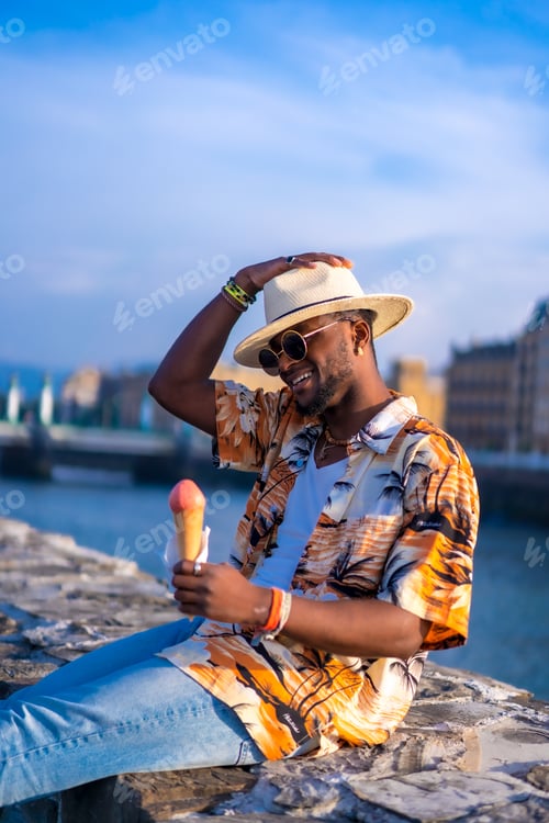 Preview: Black ethnic man enjoy summer vacation at the beach eating ice cream, sitting by the river