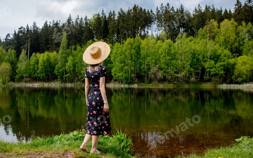 Preview: Beautiful woman in drass and hat stay next to lake in autumn time