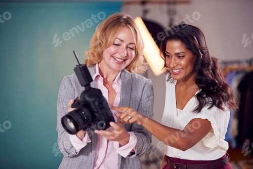 Preview: Mature Female Fashion Photographer With Client Looking At Images From Shoot On Camera In Studio