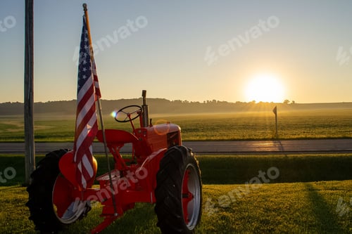 Preview: Closeup of a patriotic international Farmall tractor with the US flag at sunrise
