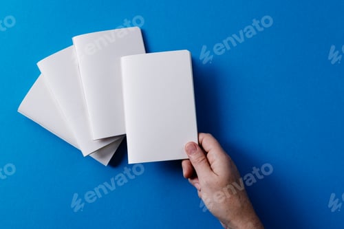 Preview: Hand of caucasian woman holding a notebook over other notebooks with copy space on blue background