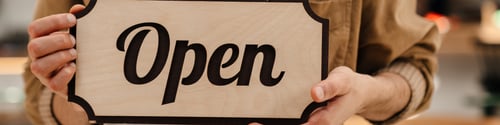 Preview: Young man waiter in apron showing open sign